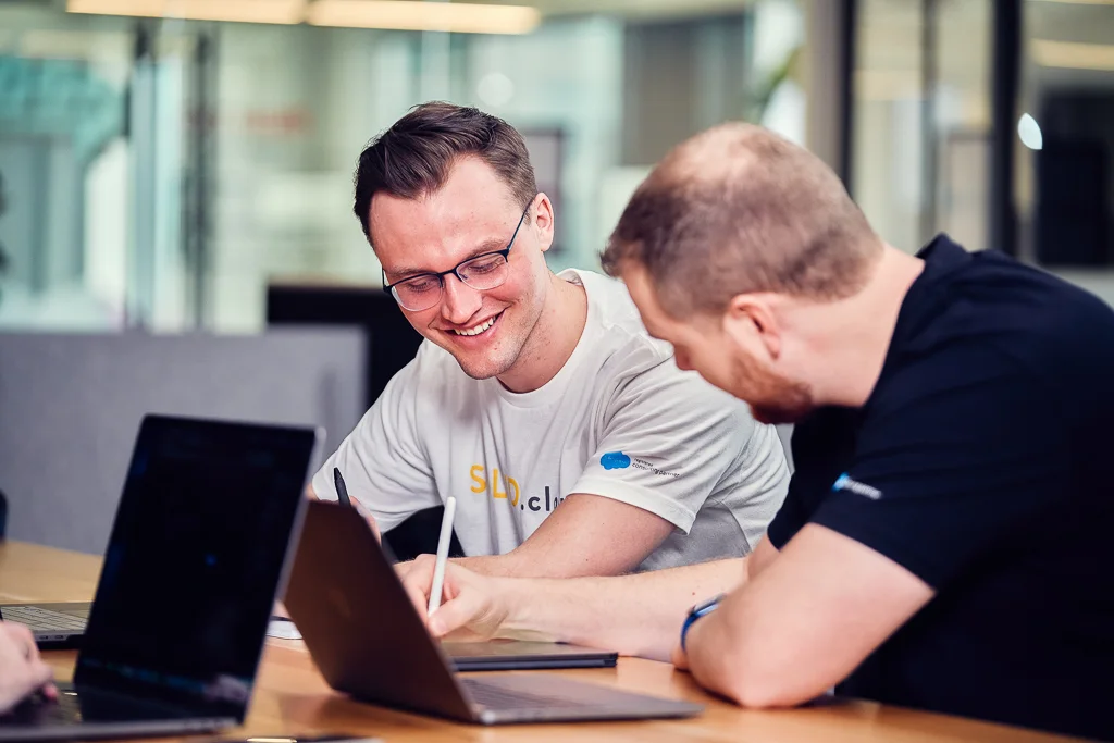 Two teammates smiling as they work through a question together at a laptop.