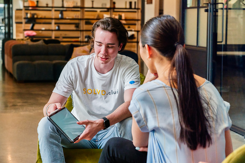 solvd employee in company logo shirt points to tablet with client in modern office